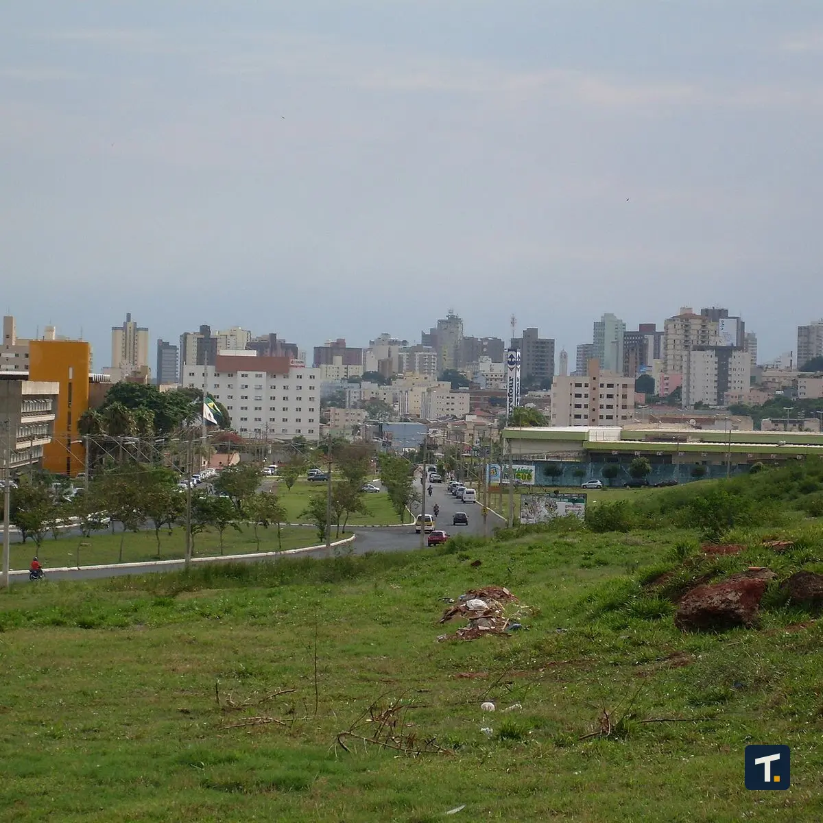 Vista de uma avenida movimentada em Uberlândia com prédios comerciais ao fundo durante o entardecer.